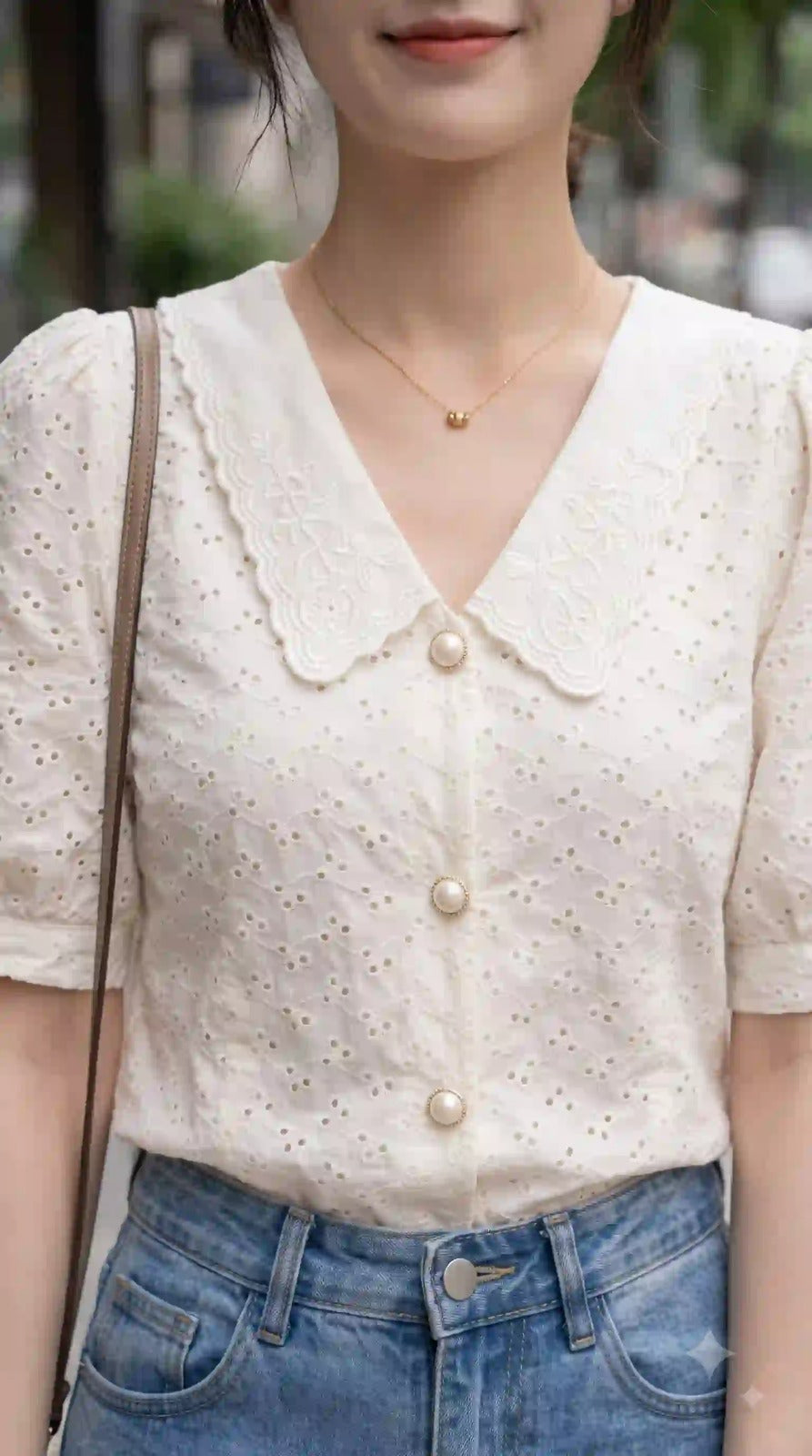 Close-up of cream eyelet top showing embroidered scalloped collar and pearl buttons